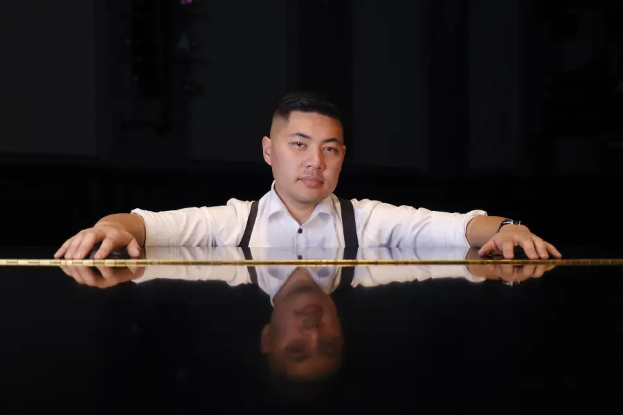 Isaac leaning on the rim of a grand piano, looking at the camera