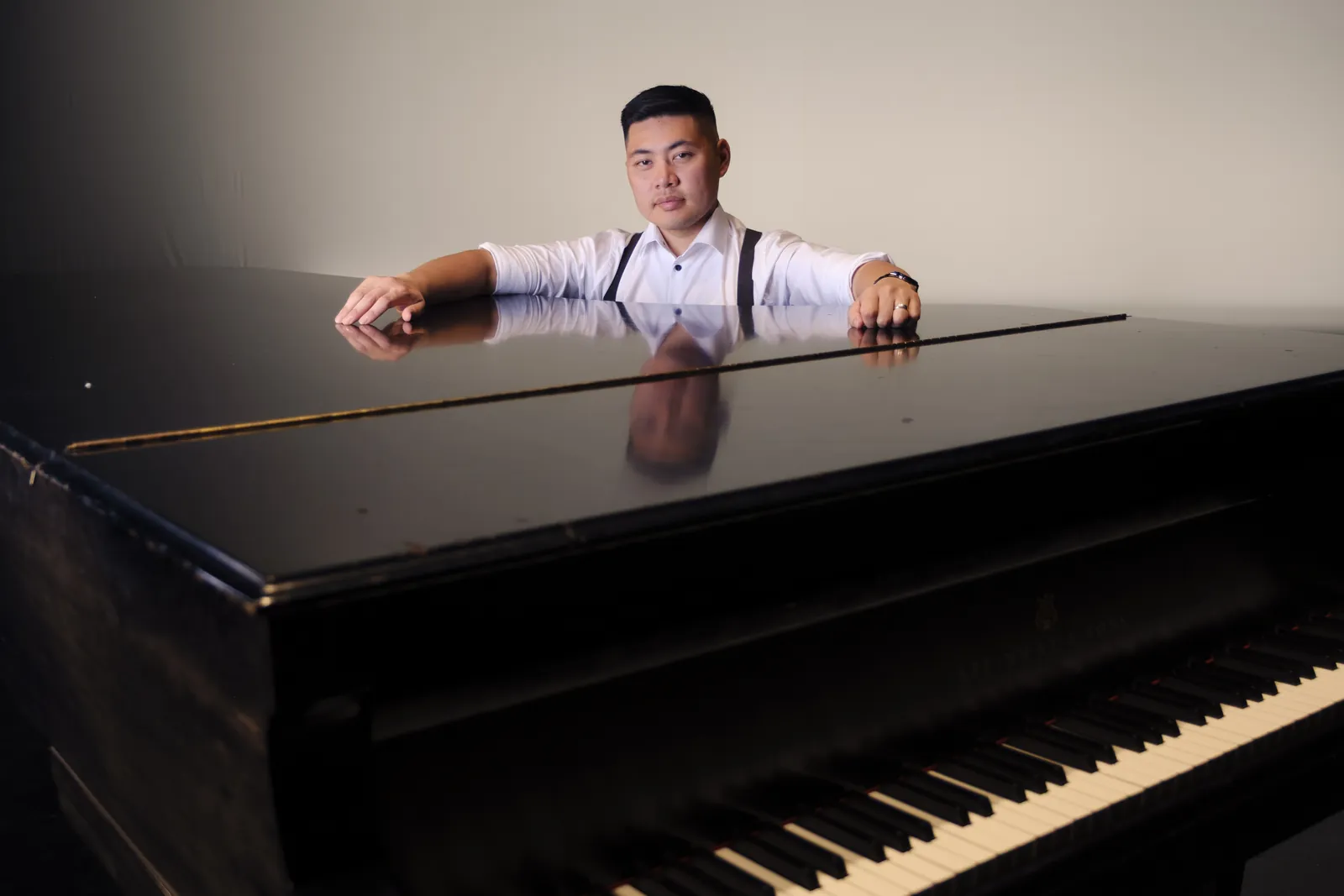 Isaac seated behind a grand piano, backlit on a dark stage