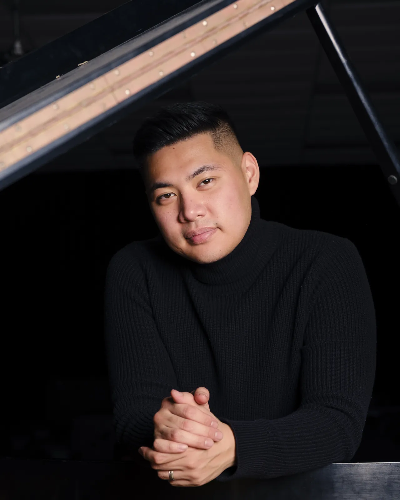 Isaac smiling, hands clasped on the piano