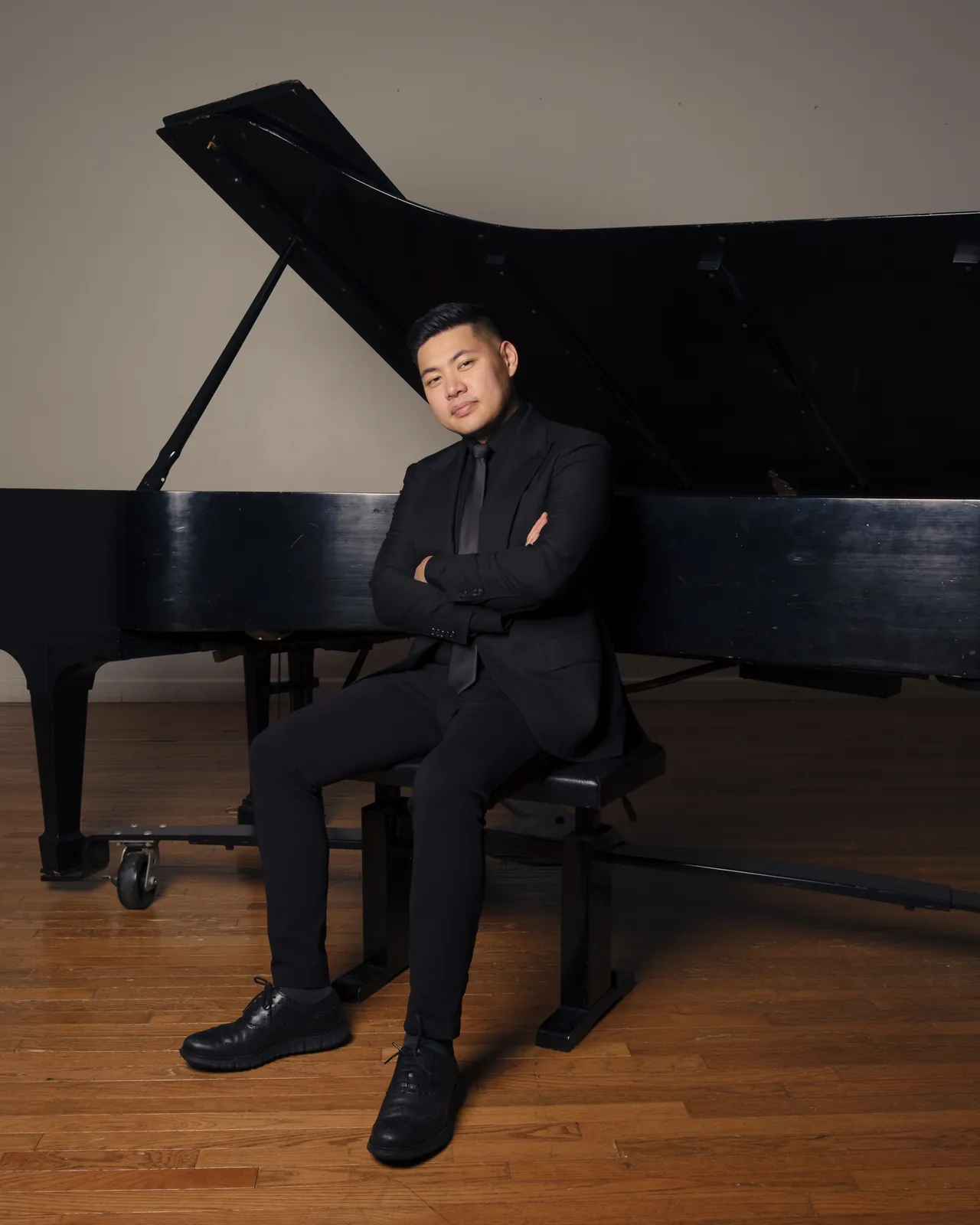 Isaac seated at a grand piano, arms crossed, in a black suit