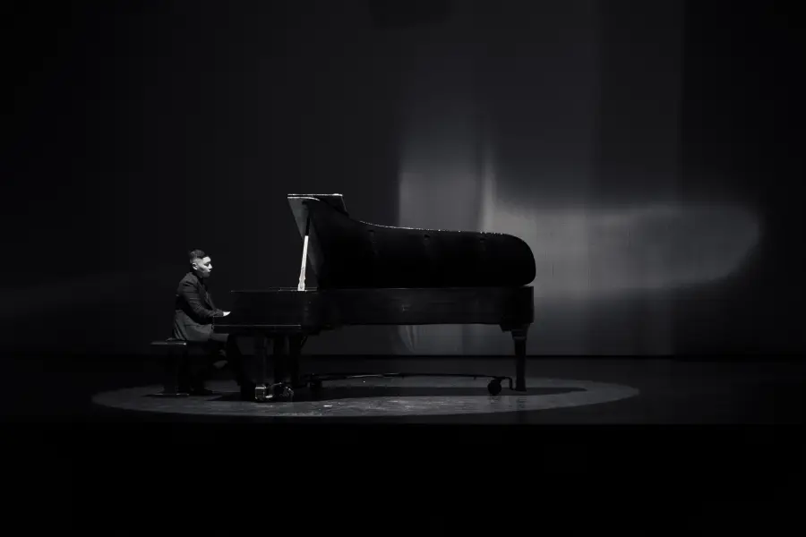 Isaac at the piano under a single spotlight